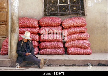 Ein älterer Mann mit traditionellem Hut liegt an einer Wand neben Säcken roter Zwiebeln in einer Straße von Celendín, Cajamarca, Peru. Stockfoto