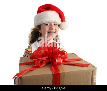 ein junges Mädchen mit Zahnspange trägt eine Weihnachtsmütze und hält ein großes Geschenk, isoliert Stockfoto