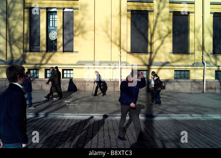 Schatten der Bäume fallen auf eine Wand der Civic Gebäude in der Nähe von dem Palast in Oslo mit Menschen zu Fuß durch in den frühen Morgenstunden Stockfoto