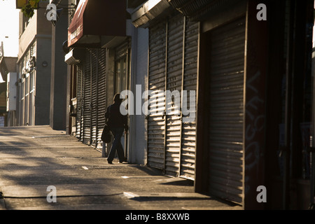 Frau tritt Tür in Zeile der gesperrten und Fensterläden Läden am Queens Boulevard Queens New York NY Stockfoto