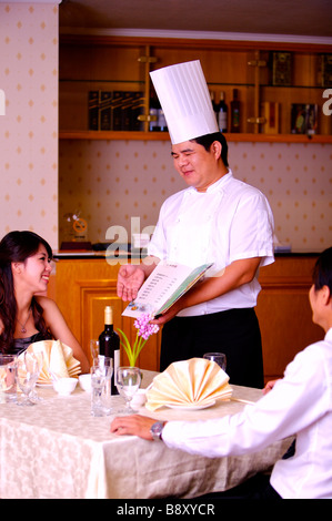 Zeigt das Menü an zwei Kunden sitzen neben dem Tisch und glücklich lächelnd Chef Stockfoto
