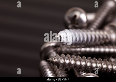 Ein Haufen Schrauben auf einem gewellten schwarzen Hintergrund. Eine Schraube hat Trockenbau Staub auf Anzeichen von unter neu aufbereitet Stockfoto