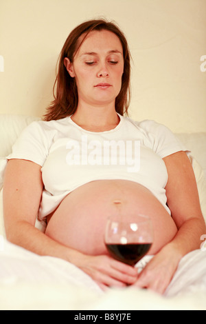 Depressive traurige hochschwangere Frau starrte bei großen Glas Rot Wein alkoholische Mama unglücklich Schwangerschaft schädlich für das ungeborene Kind Stockfoto