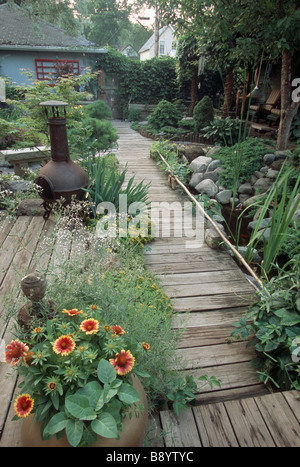 HÖLZERNEN GEHWEG DURCH MINNESOTA GARTEN IM SOMMER.  GAILLARDIA, SCHLEIERKRAUT, IRIS, KLEINER TEICH, FICHTE. Stockfoto