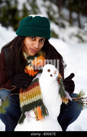 Eine Frau mit einem Hut und Schal mit einem Schneemann im Freien im Wald und Schnee. Stockfoto