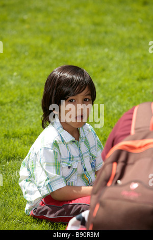 Ein kleiner Junge genießt ein Eis in der Sonne in einem Park, gekleidet in roten Hosen und ein grün-weiß gestreiften Hemd herrsche Stockfoto