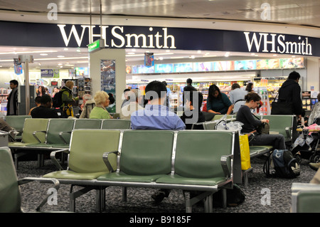 Passagiere im Innern des Flughafens London Heathrow, Terminal 3, warten in der Abfluglounge auf Anweisungen zum Einsteigen neben den WH Smith Zeitungsläden England UK Stockfoto