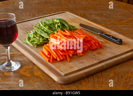 Ein Schneidebrett mit Julienne Karotten und grünen Bohnen mit einem Messer und einem Glas Wein für den chef Stockfoto