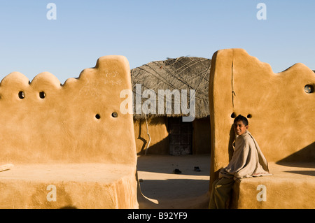 Ein Junge sitzt am Tor zu seinem schönen Haus in einem abgelegenen Dorf in der Wüste von Rajasthan, Indien. Stockfoto