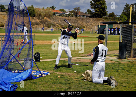 Während ein Teamkollege Kugeln wirft ein Baseball Spieler Praktiken mit der Wimper in ein blaues Sicherheitsnetz am California High school Stockfoto