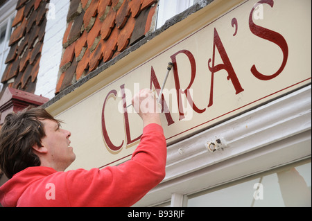 Schildermaler Keith Pettit mit einem Mahl-Stick eine Shop-Faszie in East Hoathly Malerei. Bild von Jim Holden. Stockfoto