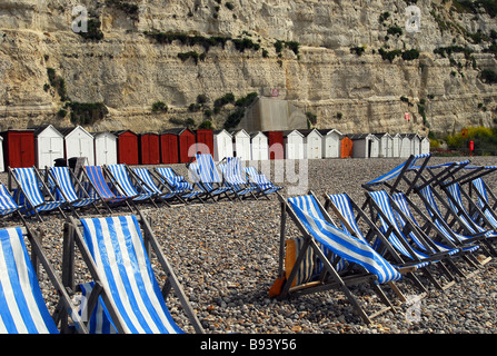 Liegestühle und Strandhütten aufgereiht auf einem einsamen Kiesstrand bei Bier mit einem schroffen Felsen drohenden hinter Stockfoto