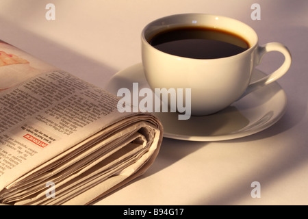 Tasse Kaffee und gefalteten Zeitung im morgendlichen Sonnenlicht Stockfoto