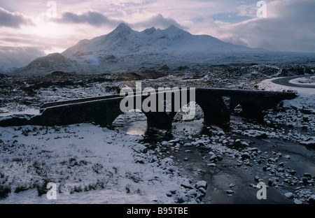 Schottland Isle Of Skye Sligachan und die Cuillin Berge im Winterschnee. Schmale Brücke über den gefrorenen Fluss und grauen Himmel. Stockfoto