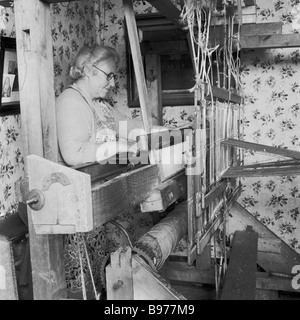 1950s, historisch, in einer Ecke ihres kleinen Häuschens, eine ältere schottische Crofter-Frau, die einen holzgerahmten Webstuhl zum Stricken von Wolle verwendete, Highlands, Schottland. Stockfoto