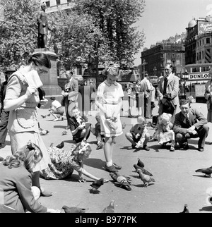 1950s, historische, sommerliche und kleine Kinder, die die Tauben auf dem Trafalgar Square, London, England füttern, beobachtet von ihren Eltern. Stockfoto