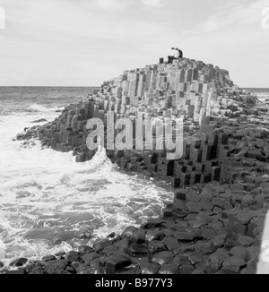 Besucher aus den 1950er Jahren sitzen auf den uralten vulkanischen Felsformationen, den Basaltsäulen, am berühmten Giant's Causeway, Antrim, Nordirland. Stockfoto