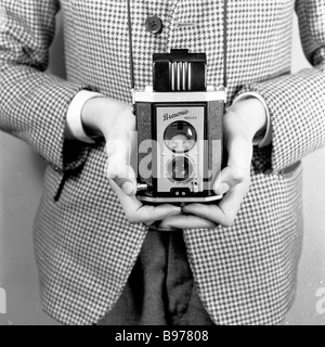 1950s, ein Junge, der demonstriert, wie man eine Kodak „Brownie“-Fotokamera mit Doppelobjektiv und Reflexionsbox hält, England, Großbritannien, mit dem Sucher oben. Stockfoto