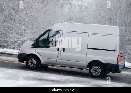 Seitenansicht eines Transitwagens, der an einem Wintertag in England auf einer schneebedeckten Straße unterwegs ist. Stockfoto