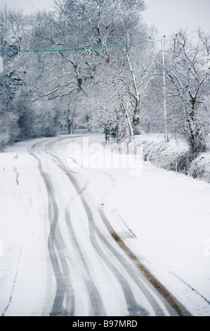 Auto Reifenspuren auf eine leere Schnee bedeckt Straße im grünen an einem Wintertag in england Stockfoto