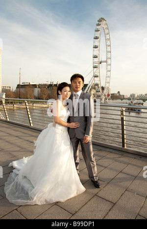 eine orientalische Braut und Bräutigam in Brautkleid und Anzug posieren vor London Eye Stockfoto