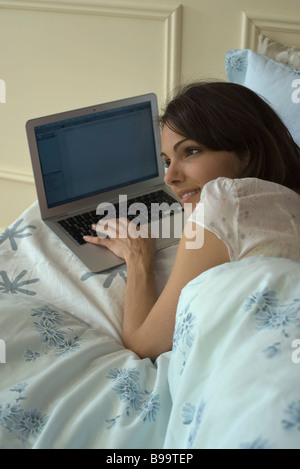 Junge Frau im Bett liegend, mit laptop Stockfoto