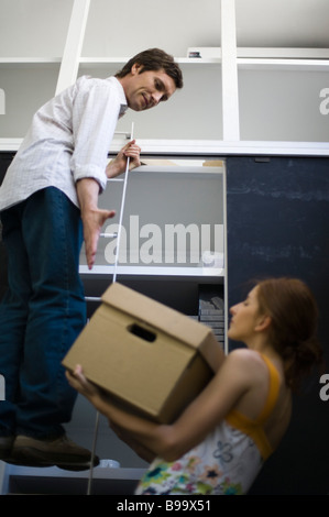 Frau, die kämpfen, um schwere Kiste bis Mann auf Leiter stehend heben Stockfoto