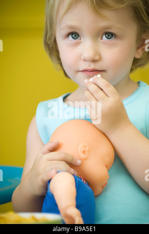 Kleines Mädchen hält Babypuppe, Essen snack Stockfoto