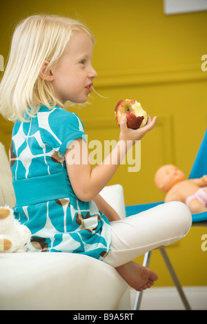 Kleine Mädchen essen Apfel auf Sofa, Seitenansicht Stockfoto