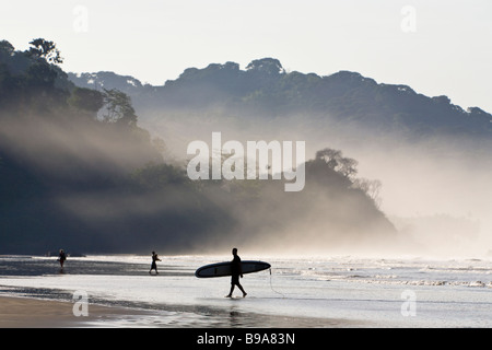 Surfer am Strand mit Sonnenlicht durch den Morgennebel am Playa Dominical in Puntarenas, Costa Rica. Stockfoto