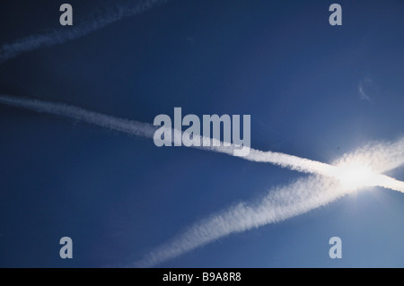 Ein Jet fliegt in die Sonne in einem Himmel voller Kondensstreifen überqueren Stockfoto