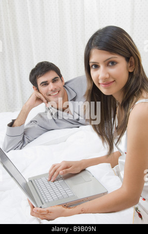 Frau arbeitet auf einem Laptop und einem Mann neben ihr liegend Stockfoto