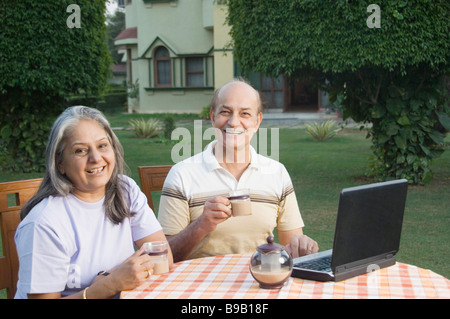 Paar mit einem Laptop und Teetrinken in einem Garten, Neu-Delhi, Indien Stockfoto