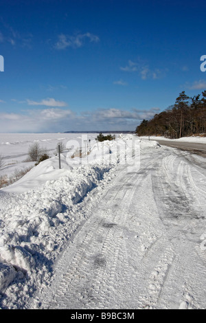 Verschneite gefrorene Lake Superior MI USA mit leerem Straßenrand der waldblaue Himmel Schnee driftet Landschaft außerhalb des Horizonts niemand verfolgt das Auto Hi-res Stockfoto