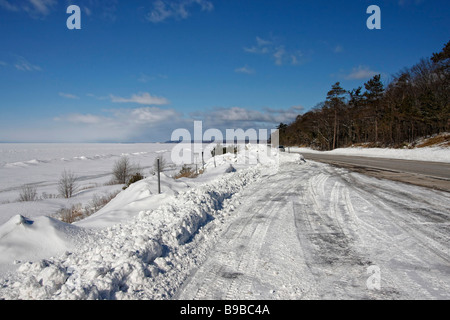 Verschneite gefrorene Lake Superior MI USA mit leerem Straßenrand der waldblaue Himmel Schnee driftet Landschaft außerhalb des Horizonts niemand verfolgt das Auto Hi-res Stockfoto