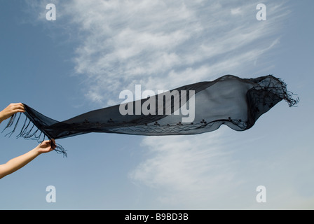 Frauenhand hält einen windumtosten schwarzen Schal Stockfoto