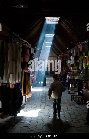 Ein Mann geht eine schmale Gasse in den Souks von Marrakesch, oder Märkten, letzten Sonnenstrahlen durchscheinen Kylights im Dach. Stockfoto