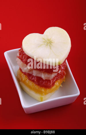 Haufen von Früchten in Form von Herzen auf rotem Grund Stockfoto