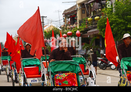 Straßenszene. Cyclo-Fahrer parade die rote vietnamesische Flagge und das Rauchen von Zigaretten. Hoi an, Vietnam Stockfoto