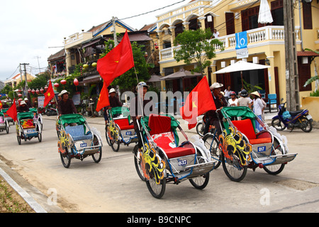 Straßenszene. Cyclo-Fahrer-Parade tragen die rote Flagge Vietnamesisch. Hoi an, Vietnam Stockfoto