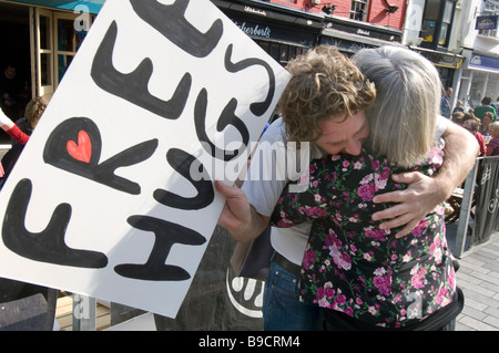 Eine Frau schmiegt sich an einen Mann mit einem Schild bietet Free Hugs Stockfoto