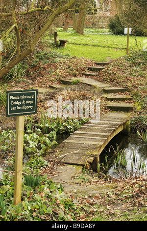 Waldspaziergang, kleine Brücke über einen kleinen Teich, Bitte beachten Sie, dass Brücke und Schritte rutschig sein können. Kleine Holzbrücke Fußweg. Stockfoto