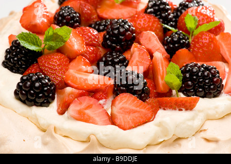 Nahaufnahme von Brombeeren und in Scheiben geschnittenen Erdbeeren, die in Schlagsahne mit frischen Minzblättern dekoriert sind. Stockfoto