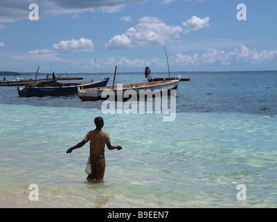 Lokale Fischer mit Handline watet im flachen Wasser aus die Insel Sansibar mit traditionellen Boote/dhows ruckartig vor Anker im Hintergrund Stockfoto