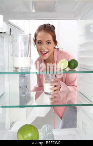 Porträt der jungen Frau, Milchglas in Kühlschrank und lächelnd Stockfoto