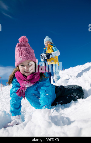 Porträt von Mädchen am Schnee liegen und lächelnd mit Junge stand im Hintergrund Stockfoto