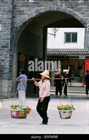 China, Provinz Yunnan, Dali Old Town. Eine lokale Frau tragen Körbe in der Nähe einer Wand Stadttor Stockfoto