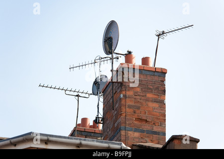 Satelliten- und Antennen auf dem Dach eines Hauses mit einem Schornstein, England, UK Stockfoto