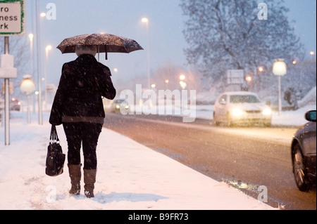 Lady Heimweg von der Arbeit entlang einer schneebedeckten Fahrbahn an einem Winter-Abend in england Stockfoto