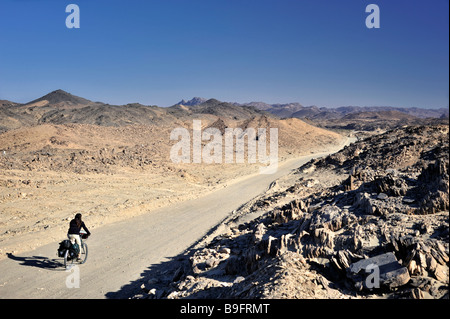 Weibliche westlichen touring Radrennfahrer mit voll beladenen Fahrrad auf unebenen Straße in der Wüste von Nubien in Nord-Sudan, Afrika Stockfoto